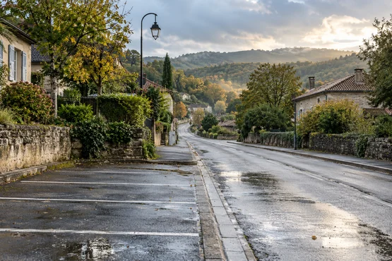 Route locale bordée de maisons et de collines sous un ciel couvert