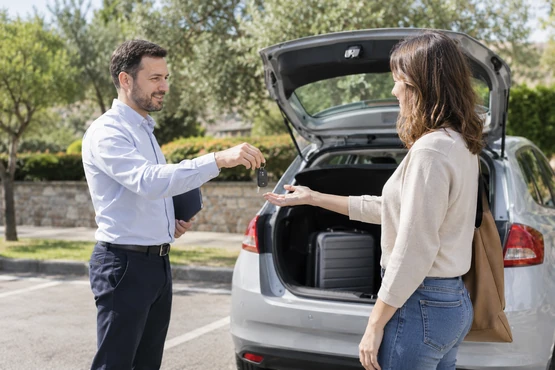 Une remise de clés près d’une voiture au coffre ouvert contenant une valise