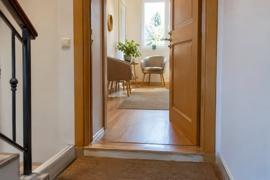 Une porte en bois ouverte donne sur un petit couloir et un espace avec deux fauteuils