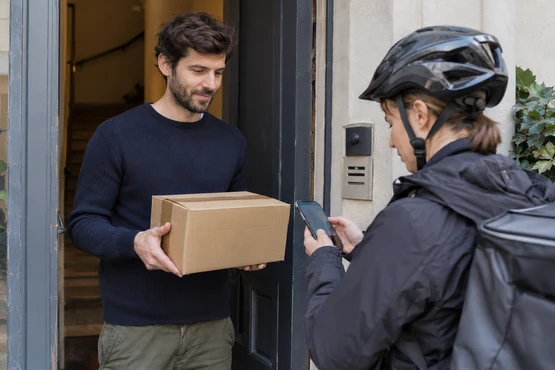 Un destinataire tient son colis pendant qu’un coursier consulte un téléphone.