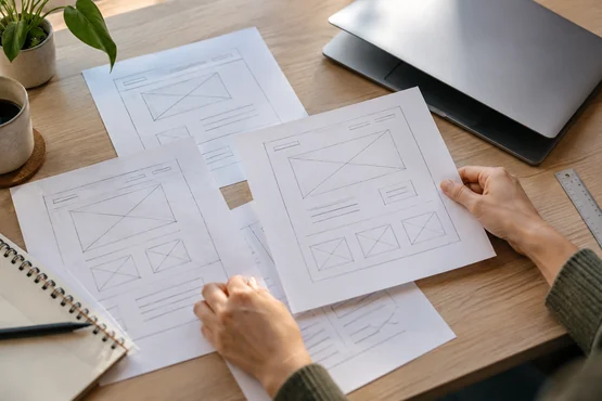 Mains d’une personne organisant des esquisses de pages web sur un bureau