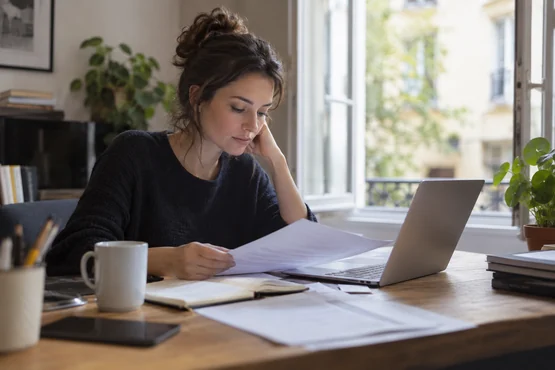 Rédactrice travaillant près d’une fenêtre avec un carnet et un ordinateur