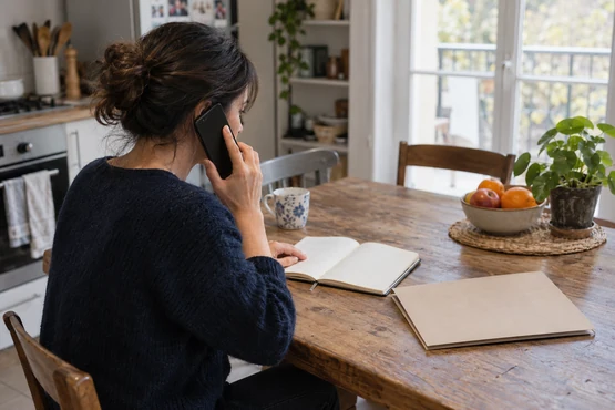 Une femme prépare un appel avec un carnet et un dossier posés sur une table.
