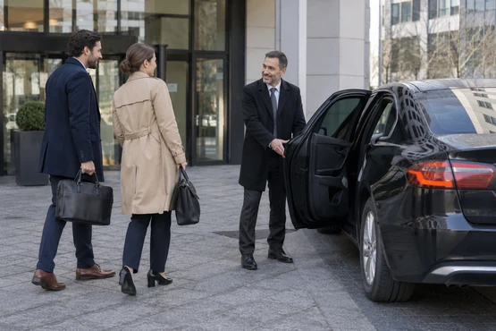 Deux collègues avec leurs sacs rejoignent un conducteur devant une entrée de bureaux.