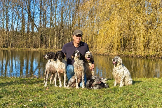 Homme entouré de plusieurs chiens sur une pelouse près d’un plan d’eau