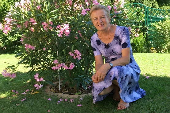 Régine Alex dans un jardin fleuri, vêtue d’une robe violette à motifs
